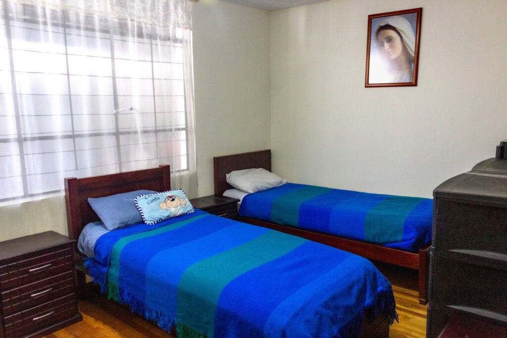 Habitación compartida de residencia geriátrica con camas, mesas auxiliares y mobiliario.